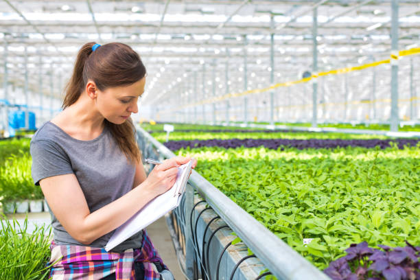 متخصص گیاهشناسی در حال یادداشتبرداری و تحلیل دادهها در گلخانه - نماد تحلیل بازار گلخانه و افزایش سودآوری