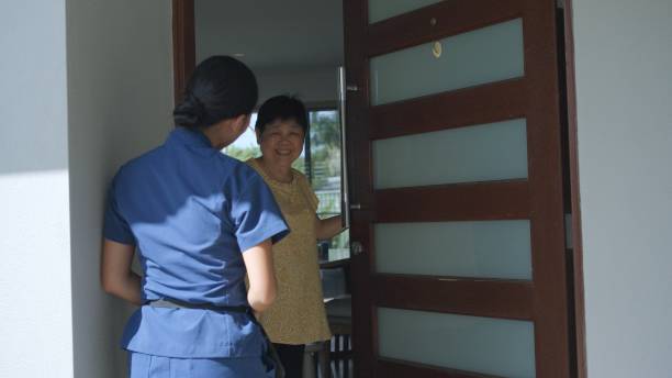 کارشناس مراقبتهای بهداشتی آسیایی در حال ورود به خانه بیمار برای ویزیت، نمادی از اهمیت دسترسی و ارتباط امن در معماری اعتماد دیجیتال