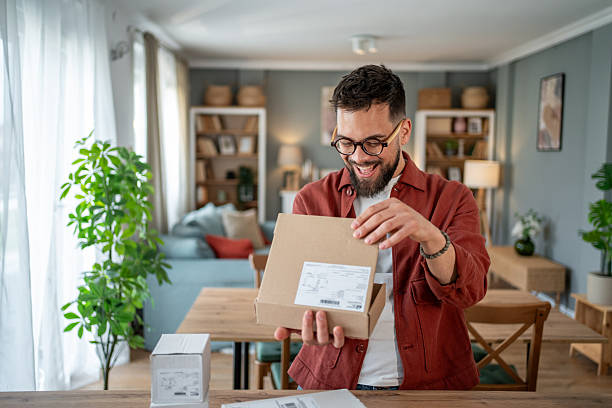 مردی خوشحال در حال باز کردن بسته محصول در خانه، نمادی از رضایت مشتریان از کیفیت و اصالت کالا – تضمین اصالت کالا در صادرات، تضمین کیفیت محصول
