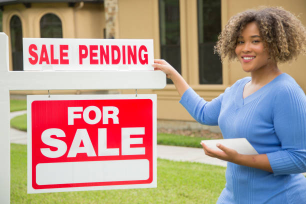 خانم جوان مشاور املاک کنار تابلوی فروش در حیاط خانه، نمادی از جذب پروژههای ویلاسازی لوکس و بازاریابی املاک