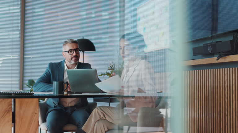 تیم اداری و تجار با لپتاپ در حال بحث و گفتگو درباره گزارشهای حسابداری و حسابرسی، که نمادی از اهمیت همکاری و دادهها در معماری اعتماد دیجیتال و شرکتهای حسابرسی است.