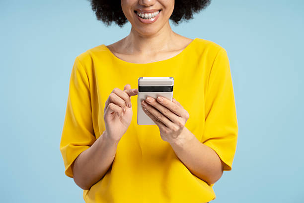 زن جوان آفریقایی-آمریکایی در حال استفاده از تلفن هوشمند روی پسزمینه آبی، نمادی از جستجوهای محلی و اهمیت سئو کلینیک دندانپزشکی برای جذب بیماران در اهواز