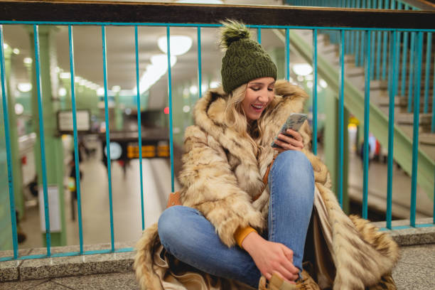 دختر جوانی در حال استفاده از تلفن همراه در ایستگاه مترو – اهمیت واکنشگرایی وبسایت برای کارخانجات کاشی