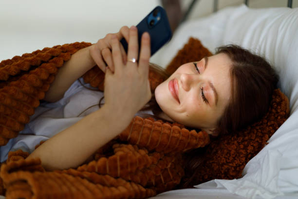 سئو پوشاک زمستانی و بازاریابی دیجیتال D2C - دختری که در رختخواب و زیر پتو با تلفن خود کار میکند