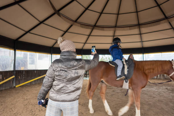 مادر جوانی که با موبایل از فرزند خود در حال تمرین با اسب فیلم میگیرد - تور مجازی اسب، فناوری VR اسب، معرفی اسب ترکمن
