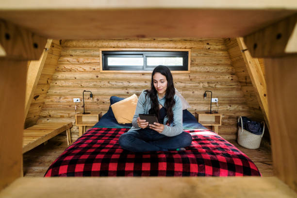 زن جوانی که تبلت به دست روی تخت خواب دنج نشسته است - تجربه کاربری اقامتگاه و فناوری در بومگردی