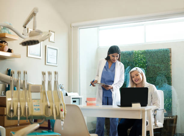 تصویر دندانپزشک در حال نمایش اطلاعات CRM پزشکی بر روی لپتاپ - مدیریت مطب دندانپزشکی و سوابق بیمار