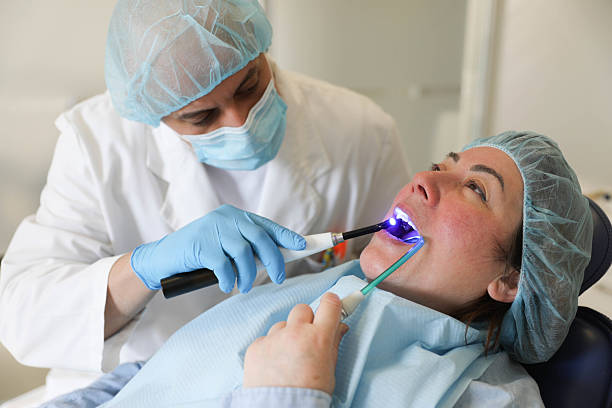 طراحی سایت پزشکی پیشرفته و سئو تخصصی برای دندانپزشکی زیبایی در کرج: افزایش Visibility و جذب مراجعین - دندانپزشک در حال درمان بیمار با نور آبی