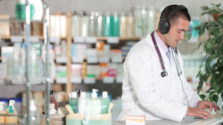 داروساز مرد با هدفون در حال بررسی اطلاعات در کامپیوتر - توسعه وب داروخانه در کرج