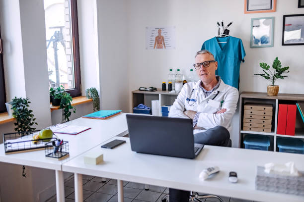 پزشک مرد تنها در مطب خود که از لپتاپ برای یک جلسه آنلاین استفاده میکند، مدیریت مطب پزشکان، پرتال نوبتدهی آنلاین