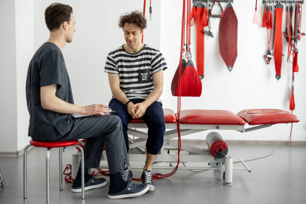 تصویر مردی در حال مشاوره با فیزیوتراپیست در مطب توانبخشی، نشاندهنده اهمیت نوبتدهی هوشمند در کاردرمانی و گفتاردرمانی