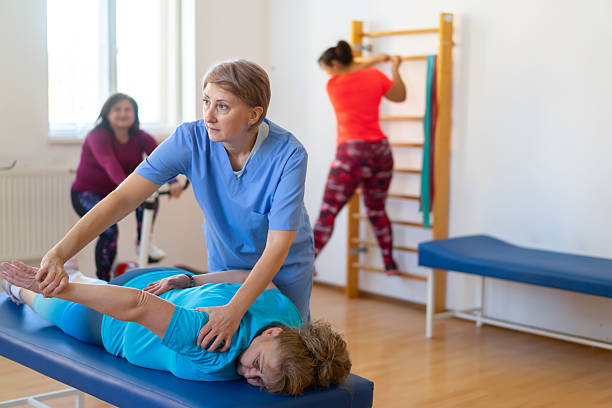 متخصص فیزیوتراپی در حال انجام حرکات کششی پا برای بیمار - توانبخشی جسمی و فیزیوتراپی