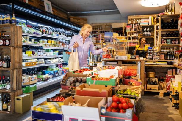 خرید و فروش عمده فرآورده‌های غذایی: زن در حال خرید گوجه فرنگی از یک خواربارفروشی در فروش‌یاب