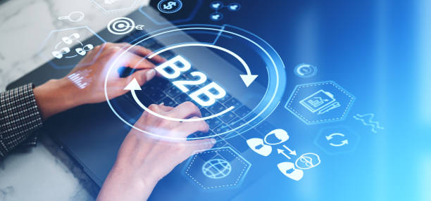 فروش‌یاب: سامانه B2B و پلتفرم خرید و فروش عمده، دست‌های یک زن تاجر در حال تایپ روی لپ‌تاپ با آیکون‌های هولوگرام B2B