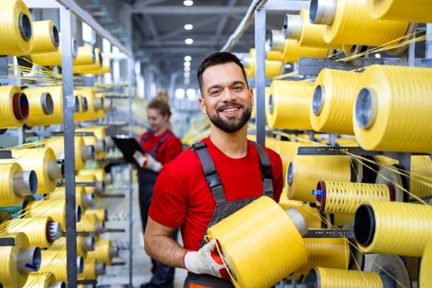 فروشیاب: خرید و فروش عمده آسان، کارگر صنعت نساجی در حال نگه داشتن دوک نخ کنار ماشین بافندگی