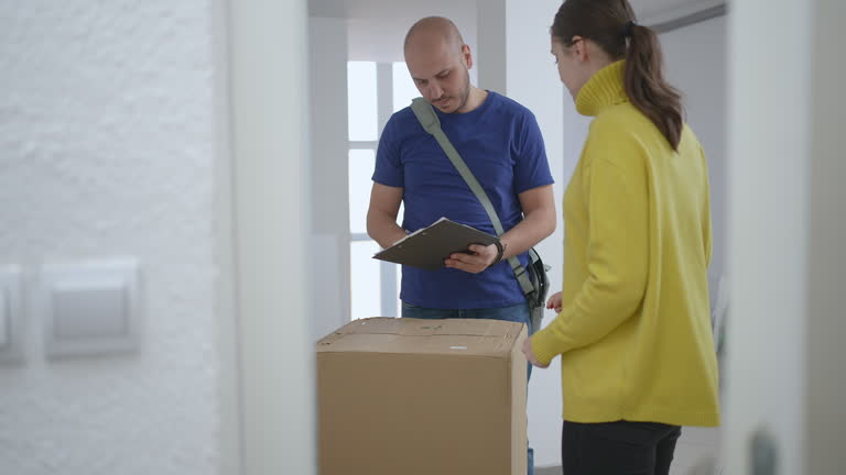 مرد تحویل‌دهنده منتظر امضای مشتری زن برای تحویل بسته - تحویل فوری خانه پیش ساخته