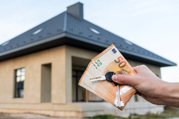 دست در حال نگه داشتن کلید و پول در مقابل پروژه ساخت خانه - خرید ویلا پیش ساخته